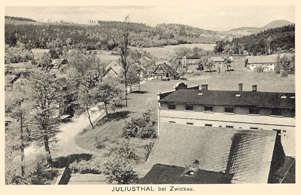 Auf dieser Ansichtskarte sieht man Juliovka (Juliusthal) vom Südosten. Das Gebäude der Weberei im Vordergrund brannte 1944 ab und bis heute sind von ihm nur im Gebüsch am früheren Spielplatz verborgene Reste der Grundmauern übrig. Im Hintergrund ist die Häusergruppe an der Strassenkreuzung, unter denen das ehemalige Knobloch'sche Gasthaus mit Tanzsaal hervorsticht. Am Horizont rechts sieht man den Berg Luž (Lausche).