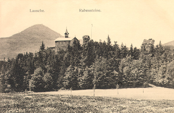 Diese Ansichtskarte zeigt eine Gesamtansicht der Felsen an den Krkavčí kameny (Rabensteine). In der Mitte sieht man die Anhöhe mit dem kleineren Felsen und dem ehemaligen Gasthaus auf böhmischem Gebiet, während der rechts stehende Felsenturm des Falkensteins sich schon auf deutschem Gebiet befindet. Am Horizont links ist der Berg Luž (Lausche).