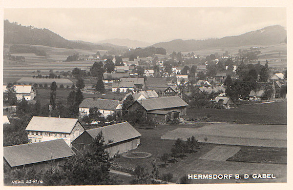 Auf dieser Ansichtskarte sieht man Heřmanice (Hermsdorf) vom Hügel Březina (Heidebüschel) am Ostrand des Dorfes gesehen. Im Hintergrund ragt der Zámecký vrch (Schlossberg) empor.