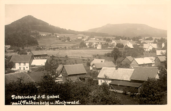 Auf dieser Ansichtskarte aus der Zeit zwischen den Weltkriegen sieht man den Südteil von Petrovice (Petersdorf) mit seinem barocken Glockenturm (Mitte). Hinter der Gemeinde links erhebt sich der Sokol (Falkenberg) und hinter ihm der Hvozd (Hochwald).