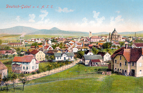 This picture postcard from 1913 shows Jablonné v Podještědí as seen from the south. In the foreground there is the road leading to Mimoň, the most prominent buildings in the town are the cathedral of St. Laurentius and St. Zdislava with its dome and the former church Birth of the Virgin which after the conflagration of the town in 1788 was reconstructed and converted to a brewery. The horizon is closed by the hills Hvozd (german: Hochwald) and Sokol.
