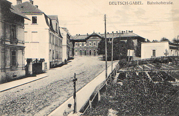 Auf dieser Ansichtskarte sieht man die aus der Stadt zum Bahnhof, dessen Gebäude in Hintergrund hervorsticht, führende Gasse. An der linken Seite stehen die Gebäude der damaligen Rautenstrauchs Fabrik und rechts befand sich eine Gärtnerei.