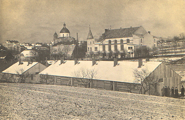 Auf dieser Ansichtskarte sieht man das Schiesshaus mit dem Dom des hl. Laurentius und der hl. Zdislava im Hintergrund. Die Holzbarracken im Vordergrund gehörten zum Internationslager in Lada (Laden) und dienten als Offiziersunterkünfte.