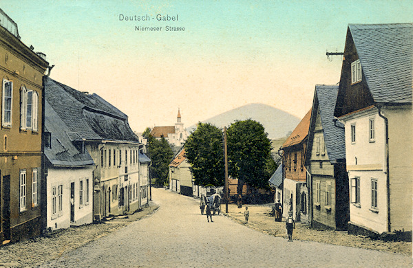 Diese Ansichtskarte zeigt die heutige Lidická ulice (Niemeser Strasse), die aus der Stadt nach Mimoň (Niemes) führt. Im Hintergrund steht die evangelische Kirche und am Horizont ragt der Tlustec (Tolzberg) empor.