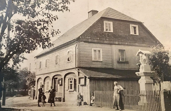 Das Foto aus dem Jahr 1938 zeigt die ehemalige Bäckerei von Johann und Franziska Ackermann im Zentrum des Dorfes. Das Haus steht nicht mehr, aber die Statue des gegeißelten Christus von 1730 ist noch erhalten.