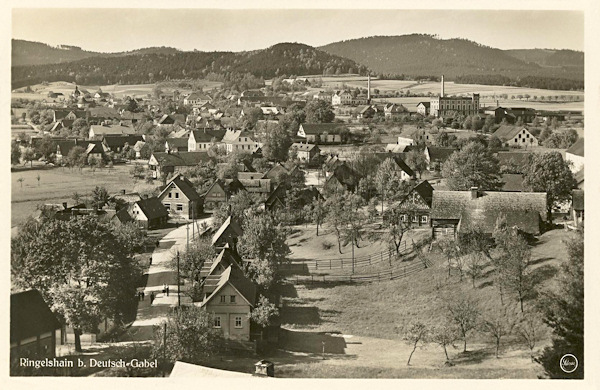 This picture postcard from 1932 shows the village from the south side. In the foreground we see the road to Janovice, in the background rises the prominent building of Schicht's soap factory and the horizon is closed by the ridge of the Lusatian hills with the prominent Pískový vrch hill.