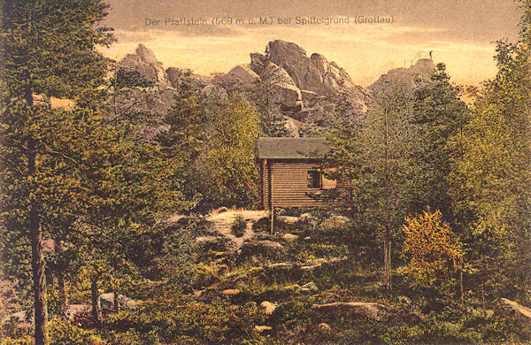 This picture postcard shows the wooden shelter „Hugo-hütte“ constructed in august 1905 beneath the Popova skála rock. In the background to the right you see the look-out peak.