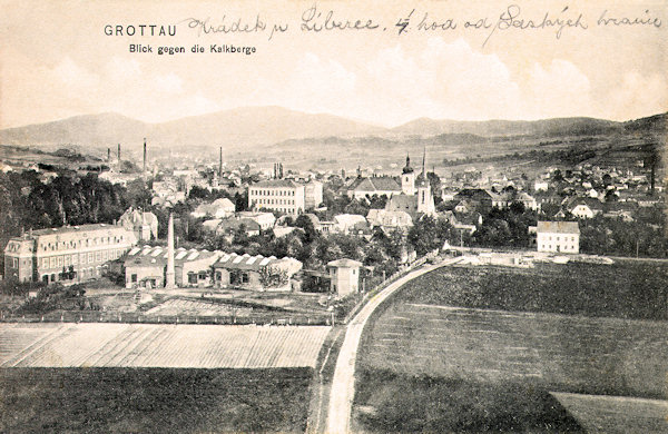 Diese Ansichtskarte von 1909 zeigt Hrádek (Grottau) aus dem Norden. Links sieht man die Fabriksgebäude in der Husova ulice (Hus-Strasse) und auf dem Felde rechts steht heute die Grundschule. Aus der städtischen Bebauung ragt der spitze Turm der evangelischen Kirche heraus, hinter ihr ist die Kirche des hl. Bartholomäus und links das monumentale Haus der Grundschule. Den Horizont schliesst der Ještědský hřbet (Jeschkenkamm) mit dem Velký Vápenný (Grosser Kalkberg) ab.