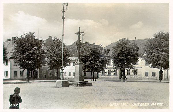 Tato meziválečná pohlednice zachycuje jihozápadní roh Dolního náměstí s centrálním Andělským křížem.