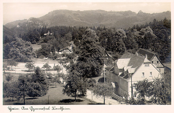 Tato pohlednice z 2. poloviny 20. století zachycuje tehdejší školní rekreační středisko v centru osady. Obzor uzavírá protáhlý masiv Töpferu se skalním ostrohem Scharfensteinu (vpravo).
