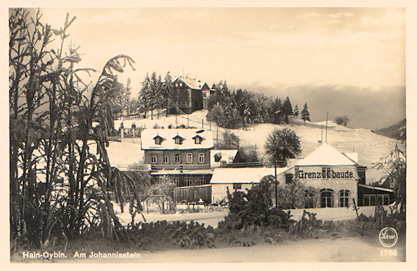 Diese Ansichtskarte zeigt die drei auf einem attraktiven Punkte an der Staatsgrenze oberhalb von Hain erbauten Gaststätten. Im Vordergrund rechts ist die deutsche „Grenzbaude“, links hinter ihr sieht man das dicht neben ihr stehende böhmische Gasthaus, das ursprünglich „Kaiser Franz Josef's-Höhe“ hiess und auf der Anhöhe im Hintergrund die Gaststätte auf den Johannissteinen (Jánské kameny). Alle diese drei Objekte stehen auch heute noch.