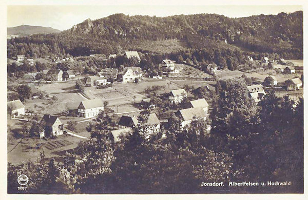 Auf dieser Ansichtskarte von 1932 sehen wir den westlichen Teil von Jonsdorf. Hinter der Gemeinde liegt das waldbewachsene Felsgebiet der Mühlsteinbrüche und im Hintergrund der Hochwald mit seinem Aussichtsturm.