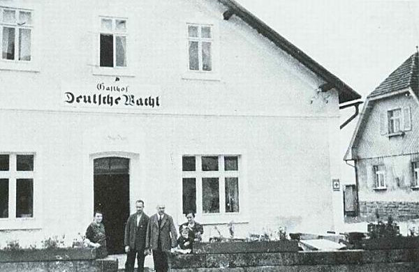 Pohled na průčelí hostince 'Deutsche Wacht' s rodinou majitele. Vpravo vykukuje budova bývalého československého celního úřadu.