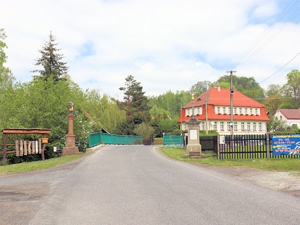 Socha sv. Jana Nepomuckého se Školním křížem na návsi. V pozadí je penzion Laguna.