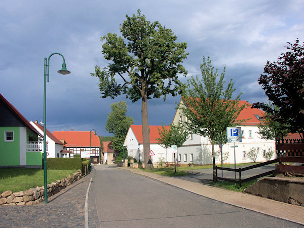 Centrum osady Alt Hartau s bývalým Školním statkem (za stromy vpravo) a hrázděnou budovou staré školy v pozadí.